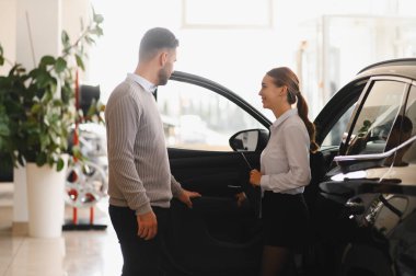 Araba galerisinde müşteri özelliklerini gösteren satıcı, satın alma seçeneklerini tartışıyor.