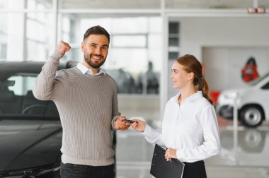 Modern bir galeride kadın bir araba satıcısından araba anahtarı alan mutlu bir adam yeni bir araba satın almayı kutluyor.