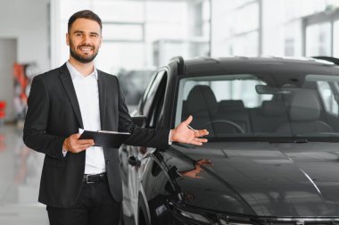 Satıcı bir araç sunuyor, bir pano tutuyor ve arabaya doğru hareket ediyor, satın alma, satış ve yardımı teşvik ediyor.