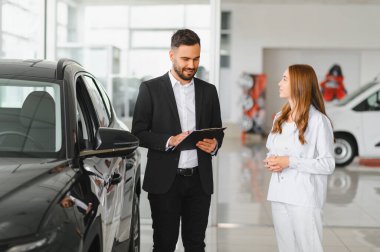 Otomotiv galerisinde kadın bir müşteriyle konuşan araba satıcısı satın almak için araç seçeneklerini sunuyor.