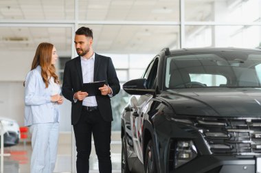 Araba satıcısı, galeride kadın bir müşteriye araç sunuyor. SUV alımı için seçenekler tartışılıyor