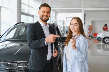 Gülümseyen araba satıcısı yeni bir araba aldıktan sonra uzaktan kumandalı araba anahtarlarını mutlu bir bayan müşteriye veriyor.