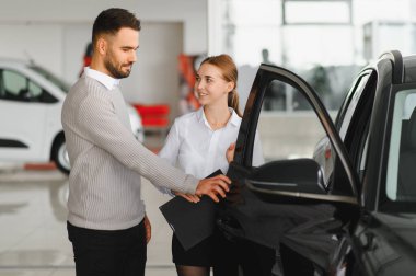 Erkek ve kadın araba satış müdürü bir aracın özelliklerini tartışıyor, yeni bir otomobil almak için seçim yapıyor.