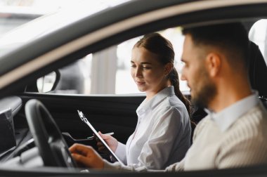 Satıcı kadın ve erkek müşteri modern bir arabanın içinde oturmuş galerideki otomobil alımıyla ilgili detayları tartışıyorlar.