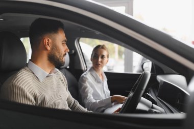 Satış elemanı satış detaylarını anlatırken yeni bir araba galerisinde oturan bir adam. Araç konsepti satın almak ve satmak