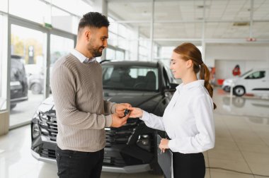 Modern bir araba galerisindeki bir satıcıdan gülümseyen ve araba anahtarlarını alan müşteri araç alımını tamamlıyor.