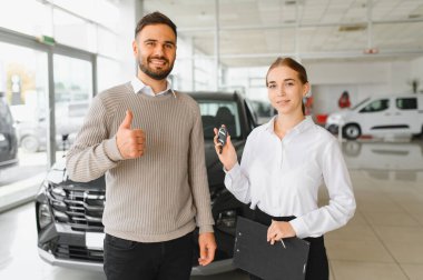 Satış elemanı galeride yeni bir arabanın anahtarlarını sunarken müşteri onay veriyor. Başarılı bir alımı kutluyoruz