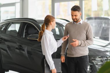 Araba satıcısı, yeni bir aracın özelliklerini modern bir galeride erkek bir müşteriye sunarak satın alma seçeneklerini tartışıyor.