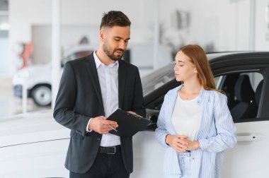 Satıcı, araba galerisinde bayan bir müşteriyle konuşuyor. Yeni bir araba alımı için evrak işlerini tartışıyor.