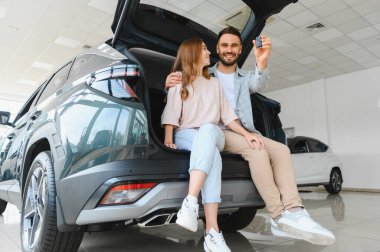 Bir galeride yeni arabalarının bagajında oturan tutkulu çift, otomobil sahibi olmayı ve özgürlüğü kutluyorlar.