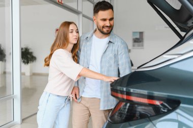 Araba galerisinde yeni bir arabaya bakan genç bir çift bir sonraki araçlarını almayı düşünüyor.