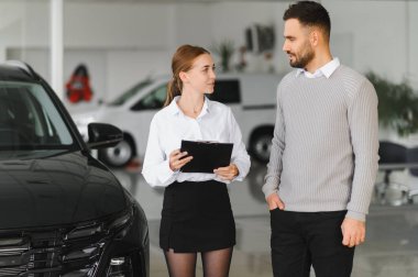 Otomobil satış uzmanı, yeni araç özelliklerini erkek bir müşteriyle tartışıyor, araba almak için bilgi ve rehberlik sağlıyor