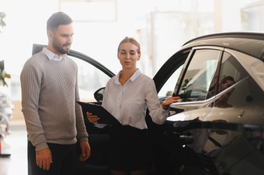 Satıcı kadın elinde bir pano, bir araba galerisinde erkek bir müşteriyle özellikleri tartışıyor. Otomotiv satış kavramı
