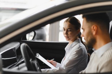Profesyonel satış temsilcisi, galeride yeni bir arabanın içinde bir erkek müşteriyle sözleşme detaylarını tartışıyor.
