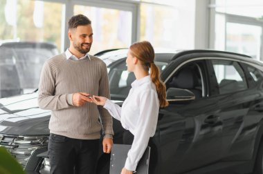 Galeri çalışanı gülümseyen bir erkek müşteriye araba anahtarı veriyor. Başarılı bir yeni araba alımını sembolize ediyor.