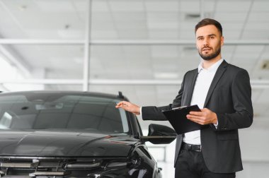 Profesyonel bir adam bir otomotiv bayisinde elinde bir not panosu olan ve satışları tartışan siyah bir araba sunuyor.