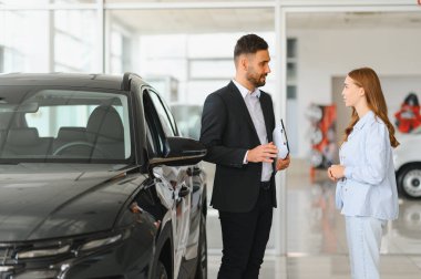 Araba satıcısı, modern bir galeride bayan bir müşteriyle konuşuyor. Yeni bir araba almaktan bahsediyor. SUV seçimi.