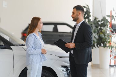 Modern bir galeride genç bir bayan müşteriye araç seçeneklerini sunan profesyonel bir araba satıcısı.