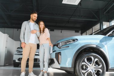 Modern elektrikli bir arabanın yanında duran mutlu çift potansiyel yeni otomobil alımlarını tartışıyor.