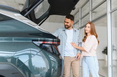 Modern bir jipin bagajını inceleyen çift, temiz bir araba galerisinden araç almayı düşünüyor.