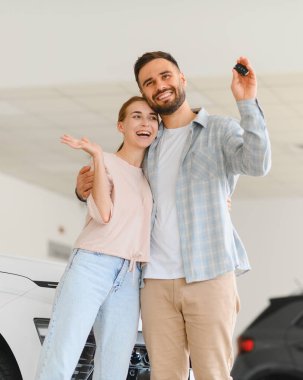 Araba alımını kutlayan, gülümseyen ve bir galeride kucaklaşan genç bir çift. Aracın anahtarını heyecanla yükselten adam