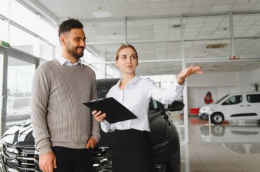 Araba seçenekleri ve özellikleri konusunda gülümseyen müşterilere rehberlik eden kadın modern bir galeride danışmanlık ve yardım sunar.