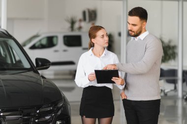 Bir araba galerisindeki müşteriyle, önemli detayların yazılı olduğu bir panoya işaret ederek, profesyonel pazarlama terimleri pazarlar.