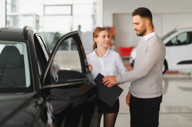 Satıcı ve müşteri gülümsüyor ve yeni bir arabanın detaylarını tartışıyor. Parlak, modern bir galeride, satın alma seçeneklerine karar veriyor.