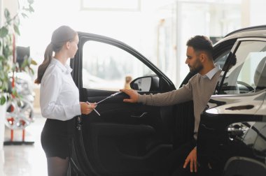 Satıcı kadın, galeride yeni bir arabanın özelliklerini keşfeden bir erkek müşteriye yardım ediyor. Araba alışverişi ve danışmanlık konsepti