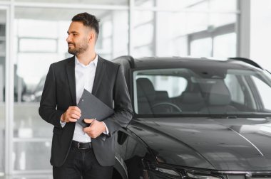 Modern, parlak bir otomobil satış merkezinde yeni araç modelleri gösteren ya da tanıtan profesyonel erkek danışman