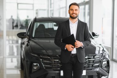 Yeni bir otomobilin önünde duran profesyonel satıcı, bir dosya tutuyor, araba satışlarını ve müşteri hizmetlerini temsil ediyor.
