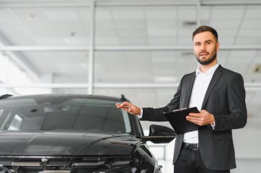 Profesyonel satıcı, galeride müşteriye araba sunar, elinde not panosu ve kalemle otomotiv sektöründe çalışır.