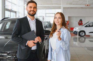 Araba galerisinde gülümseyen satıcı ve bayan müşteri, yeni araba anahtarlarıyla başarılı bir alışverişi kutluyorlar.