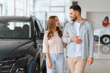 Araba galerisinde yürüyen genç bir çift yeni bir araba ya da cip almayı düşünüyor. Gülümsüyorlar ve birbirlerine bakıyorlar.