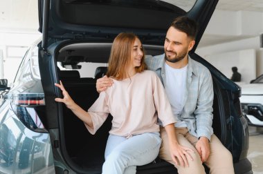 Modern bir sergi salonunda yeni araba özellikleri keşfeden genç bir çift, gelecekteki yolculukları ve alışverişleri hayal ediyorlar.