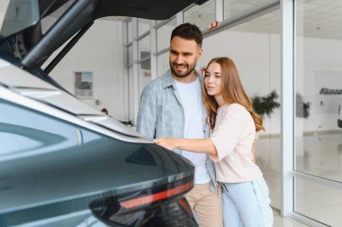 Mutlu genç çift yeni modern bir arabanın bagajını inceliyor, lüks bir galeride seçim yapıyorlar.