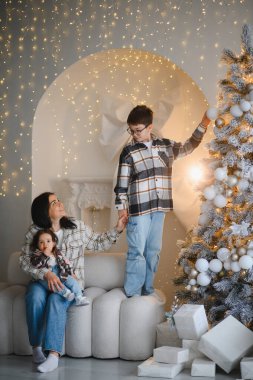 Anne kucağında bebek, büyük oğlu da Noel ağacını süslerle süslerken tatilini evde kutluyor.