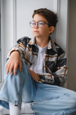 Ekose gömlekli ve kot pantolonlu genç adam pencere kenarında oturmuş, düşünüyor ve hayal kuruyor. Fikir üretmek ve yansıtmak