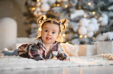 Bir Noel ağacının önünde pofuduk bir halıya uzanmış, dilini uzatıp neşeli bir tatil cazibesiyle gülümseyen tatlı bir kız.