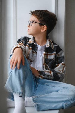 Düşünceli yüzlü çocuk pencerenin kenarında oturmuş hayal kuruyor, düşünüyor ve gençliği ve özlemleri derin düşüncelere dalıyor.