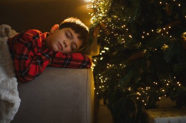 Tatil döneminde rüya gören bir çocuk, kafasını ışıklarla süslenmiş bir Noel ağacı ile dinlendiriyor.