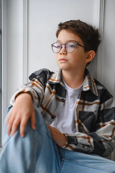 Ekose gömlekli ve gözlüklü ergen bir çocuk izliyor, yansıtıyor ve pencerenin kenarında rüya görüyor. Gençlik ilham arıyor