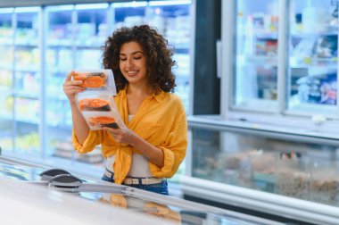 Gülümseyen, taze somon bifteği fileto tutan bir kadın markette dondurucunun yanında alışveriş yaparken.