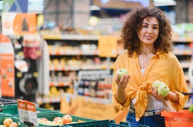 Canlı bir süpermarketten alışveriş yaparken elinde taze yeşil elmalar tutan bir kadın. Sağlıklı beslenme ve tüketici yaşam tarzı