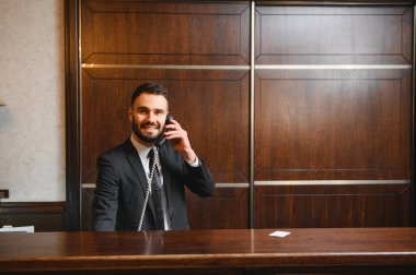 Lüks otel resepsiyonunda duran arkadaş canlısı resepsiyonist telefonda mükemmel müşteri hizmetleri sunuyor.