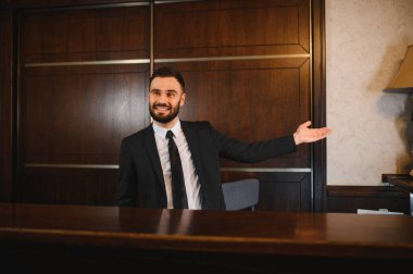 Gülümseyen adam lüks bir otel resepsiyonunda sunum yapıyor. Profesyonel bir konukseverlik gösteriyor.