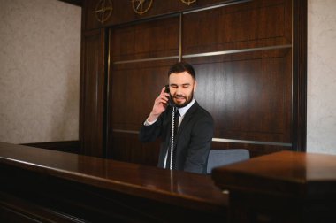Otel resepsiyonisti mükemmel misafir servisi sunuyor, ahşap bir resepsiyondan gelen telefona cevap veriyor.
