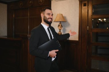 Takım elbiseli, otel resepsiyonisti olarak çalışan gülümseyen adam lobiye gelen misafirleri selamlıyor. Profesyonel hizmet sağlanıyor