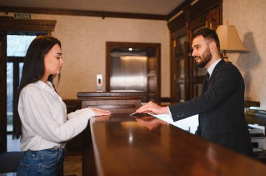 Misafir resepsiyon görevlileriyle konuşuyor, otel lobisindeki kontrolleri tamamlıyor, mükemmel bir konukseverlik hizmeti alıyor.