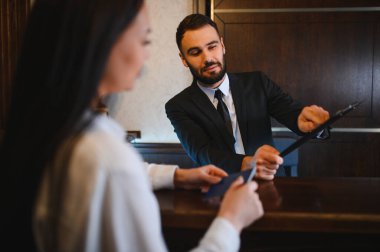 Resepsiyonist, resepsiyonist bir kadına pasaport konusunda yardım ediyor, otel lobisinde konukseverlik hizmeti veriyor.